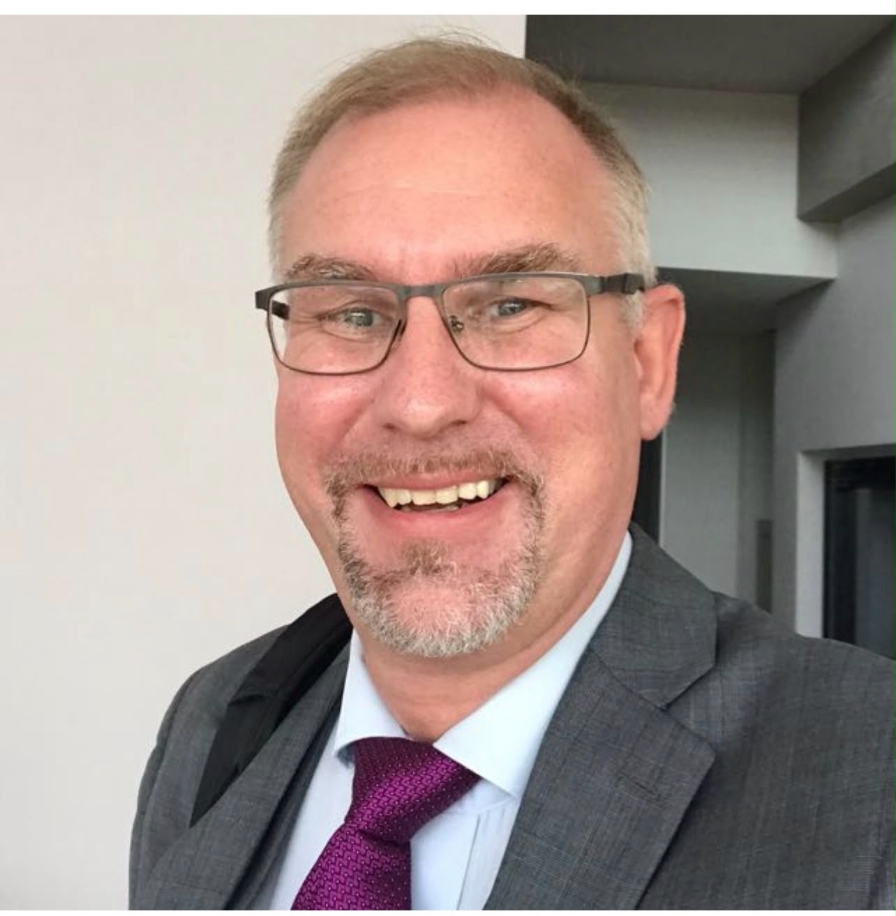 head shot of Steven Garschke - co-founder - relocate·brazil ENGLISH HOUSE wearing a grey suit, white shirt, and purple tie.